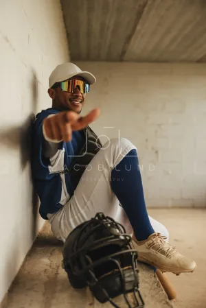 Confident baseball player in full uniform sitting in dugout pointing toward camera with a smile